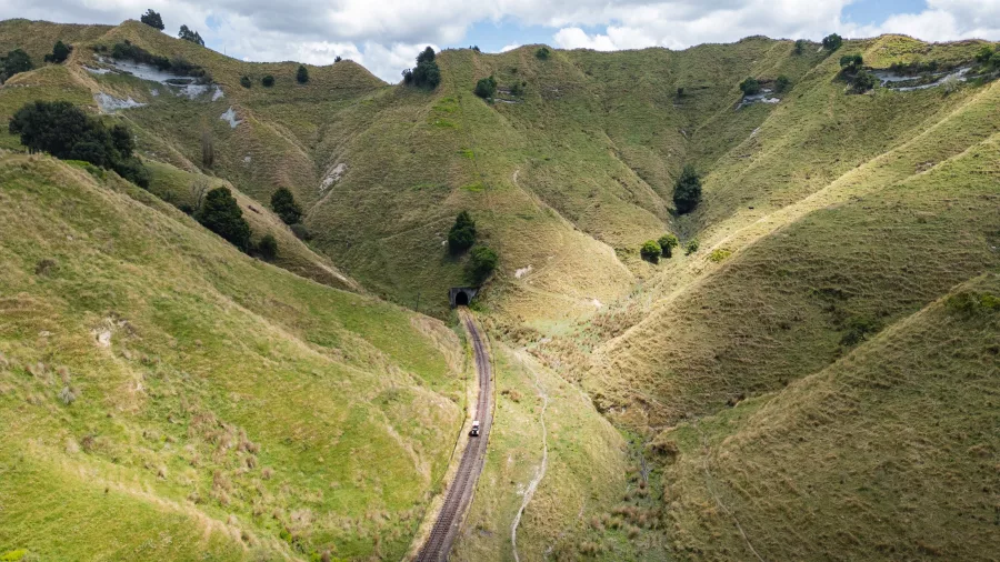 A rail cart approaches a tunnel cutting through steep, grassy hills on the Forgotten World Adventures route.