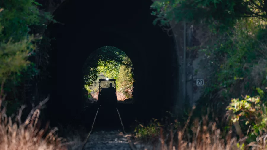 Silhouetted rail cart travelling through a dark tunnel with light at the far end on the Forgotten World Adventures tour.