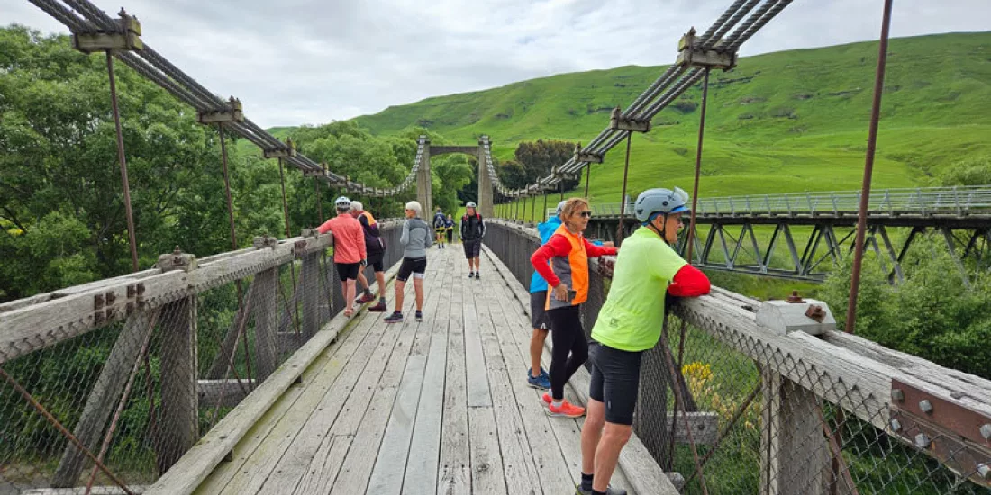 Group of cyclists taking a break on a historic wooden bridge surrounded by lush countryside