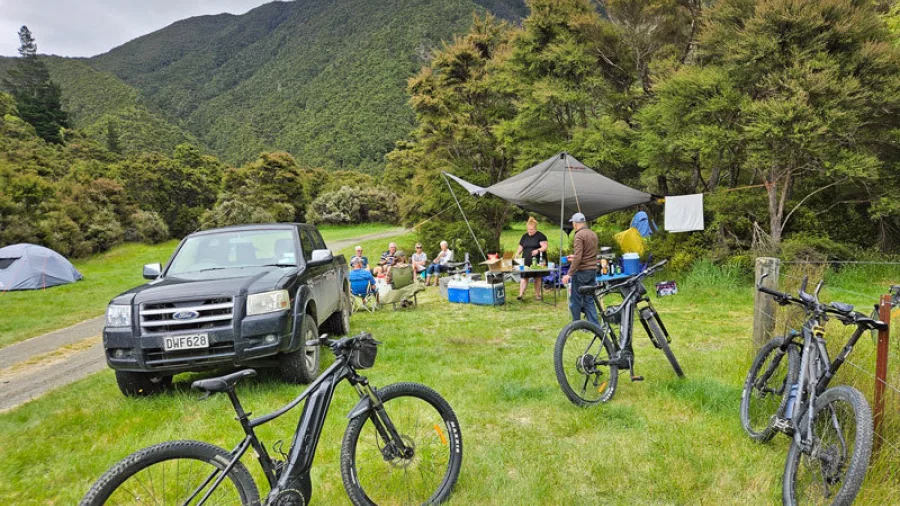 E-bikers taking a lunch break at a riverside campsite with bikes, 4WD and shelter
