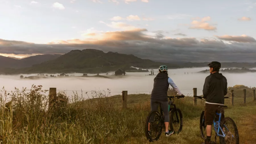 Two cyclists on E-bikes enjoying sunrise views over a mist-filled valley