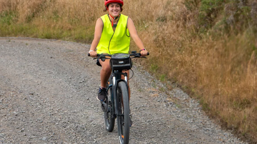 Smiling woman riding an E-bike along a gravel path through dry grassland