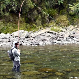 Angler standing midstream in the Rangitikei River casting a fly rod