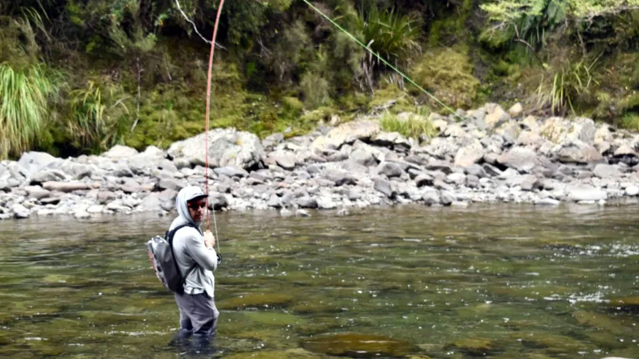 Angler standing midstream in the Rangitikei River casting a fly rod