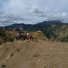 Two riders on horseback pausing along a ridgeline with vast hill country views