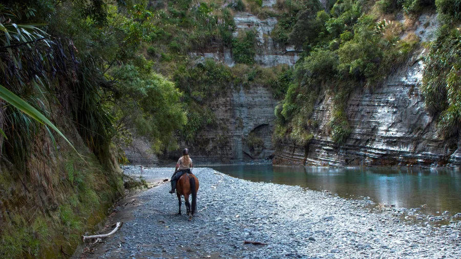 Horse rider following a stony trail beside the Rangitikei River canyon cliffs