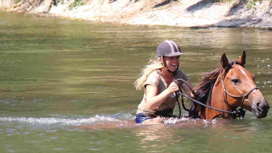 Smiling rider guiding a horse through deep water during a river swim