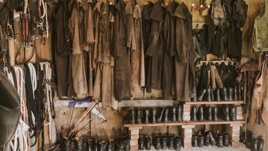 Neatly organised tack room with raincoats, saddles, and riding boots at River Valley Stables