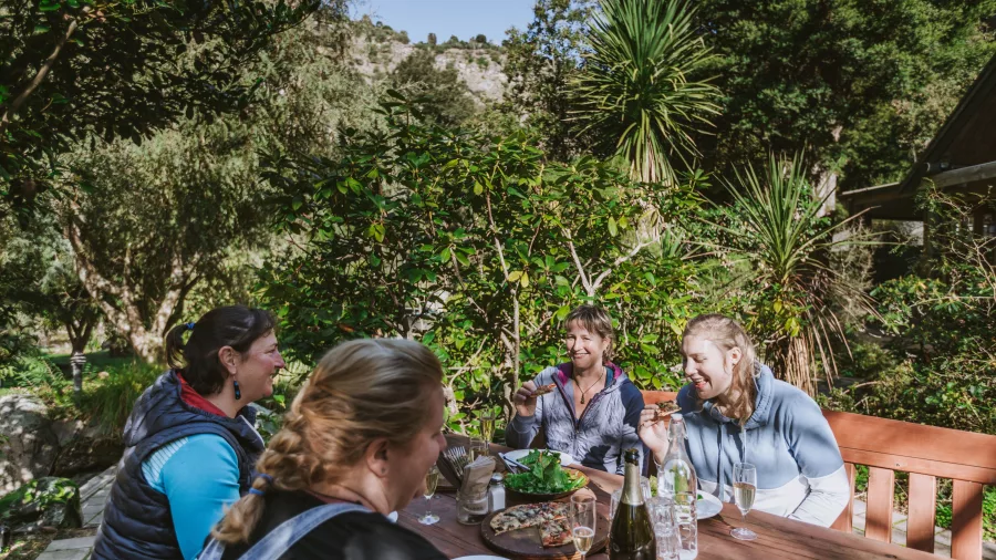 Four women enjoying lunch and wine at an outdoor table surrounded by greenery