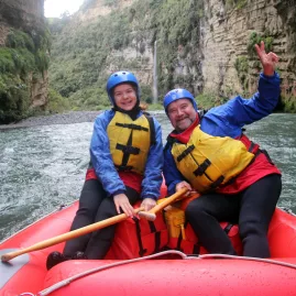 Father and daughter smiling in raft with Rangitikei Gorge cliffs behind