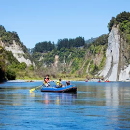 Family in a blue raft paddling along the Rangitikei River with scenic cliffs