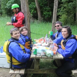 Family in rafting gear enjoying a riverside picnic lunch during the tour