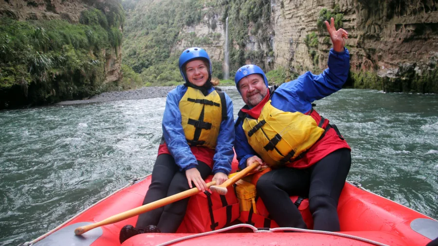 Father and daughter smiling in raft with Rangitikei Gorge cliffs behind