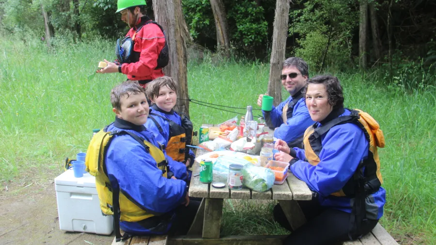 Family in rafting gear enjoying a riverside picnic lunch during the tour