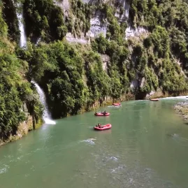 Red rafts passing beneath twin waterfalls along a lush green cliff on the Rangitikei River
