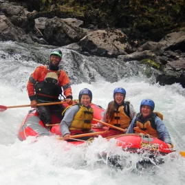 Raft guide steering a group of four down a foamy rapid in a red raft on the Rangitikei River
