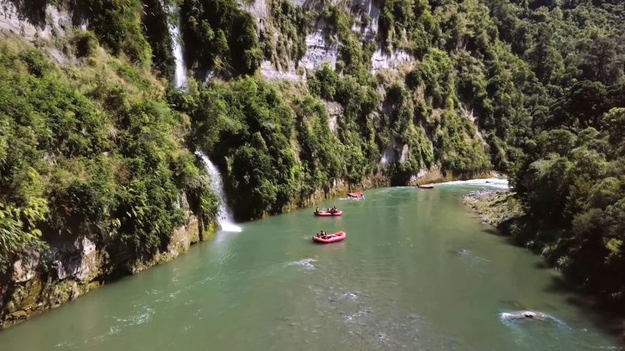 Red rafts passing beneath twin waterfalls along a lush green cliff on the Rangitikei River