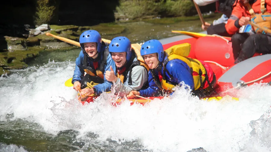 Three excited rafters bracing through waves on a red raft in Grade 5 rapids