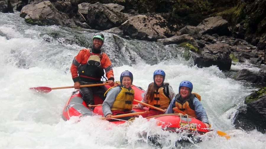Raft guide steering a group of four down a foamy rapid in a red raft on the Rangitikei River