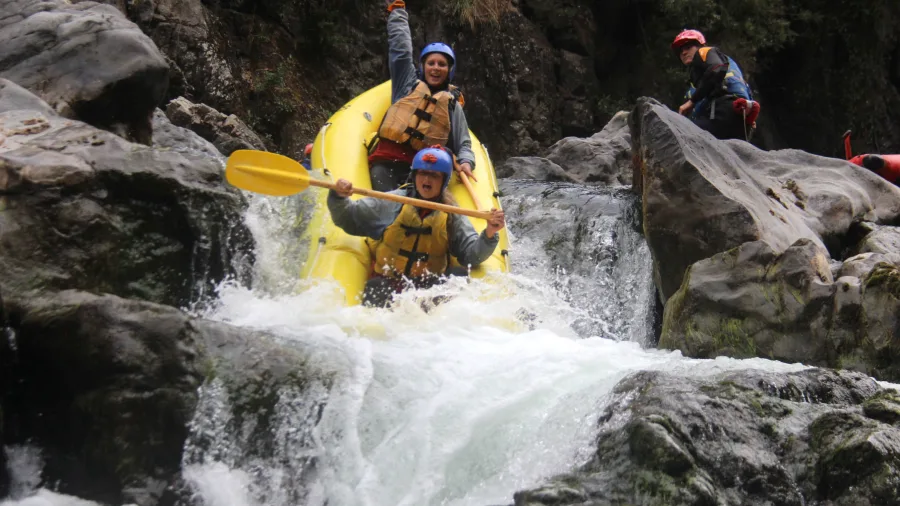 Two rafters in a red inflatable duckie joyfully descending a rocky drop on the Rangitikei River
