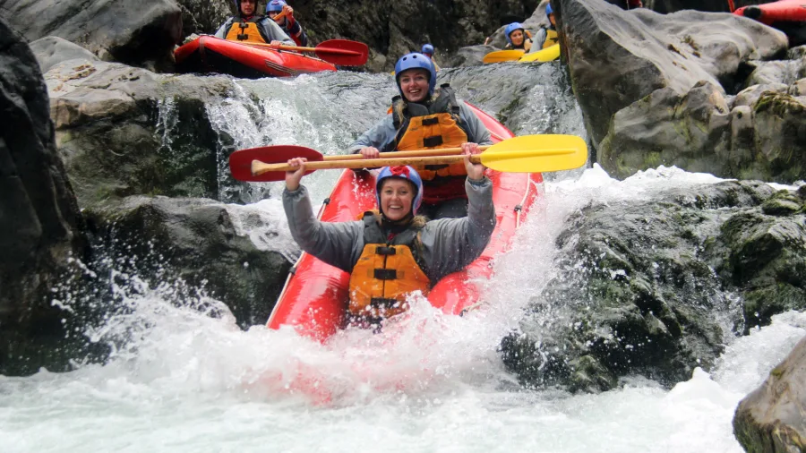 Tandem rafters in a red inflatable kayak tackling a small waterfall on the Rangitikei River