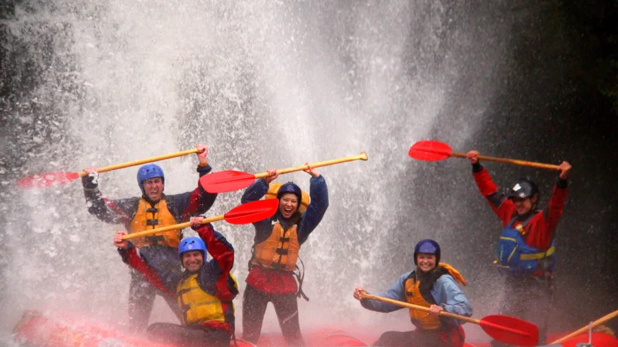 Rafting group celebrating under a powerful waterfall on the Rangitikei River in New Zealand