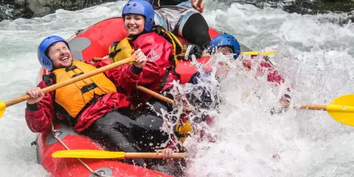 Group of rafters smiling and paddling through crashing white water rapids on the Rangitikei River