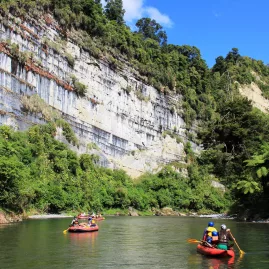 Families paddling inflatable kayaks past a tall limestone cliff on the Rangitikei River