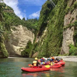 Family group in duckies paddling through steep canyon cliffs on the Rangitikei River