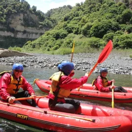 Three paddlers laughing and enjoying calm waters in inflatable kayaks on the Rangitikei