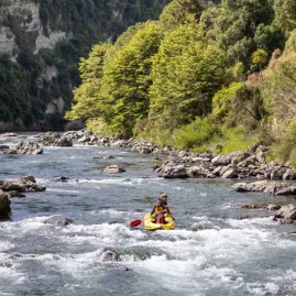 Solo paddler in a yellow inflatable kayak navigating bouldery rapids on the Rangitikei River