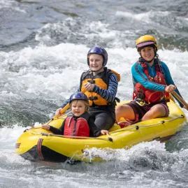 Family of three navigating gentle whitewater in a yellow duckie on the Rangitikei River