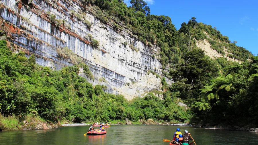 Families paddling inflatable kayaks past a tall limestone cliff on the Rangitikei River