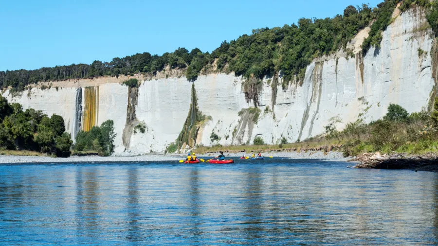 Inflatable kayaks on the Rangitikei River with white papa cliffs and a waterfall in the background