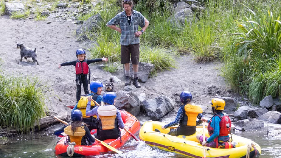 Children arriving at the riverbank in duckies while a guide and dogs look on