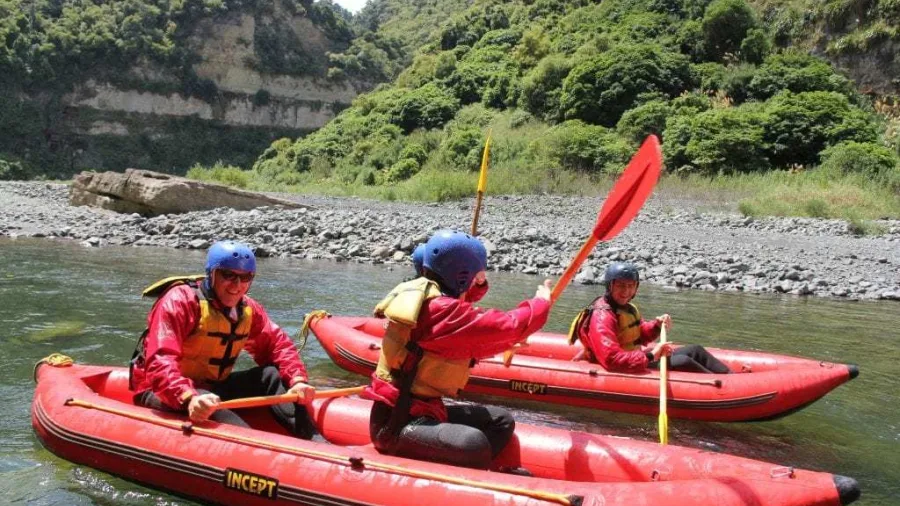 Three paddlers laughing and enjoying calm waters in inflatable kayaks on the Rangitikei