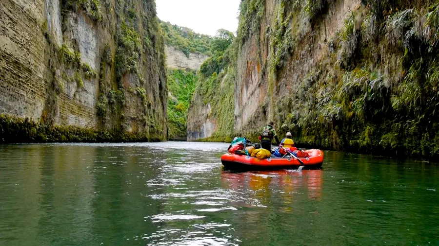 Rafting group paddling through the emerald waters and narrow canyon walls of Mokai
