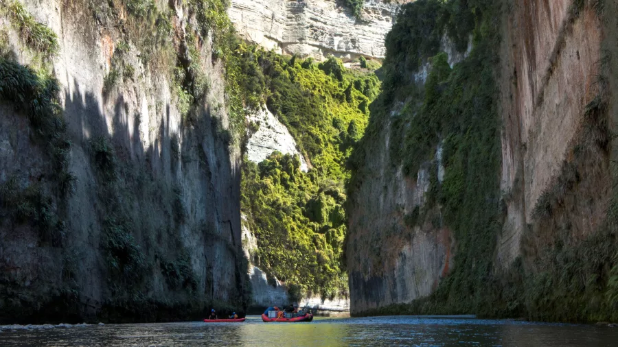 Rafts approaching a sunlit exit of Mokai Canyon with vertical cliffs and vibrant greenery