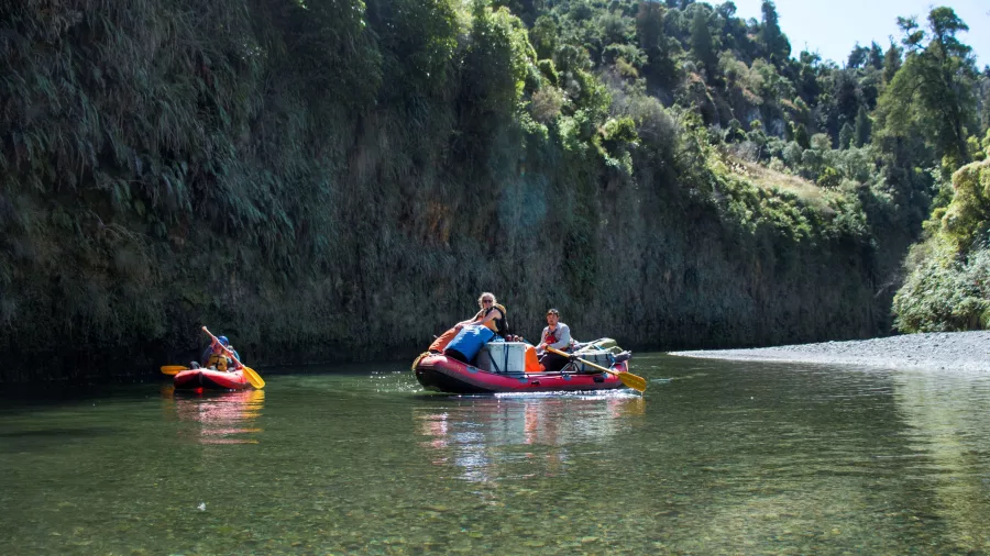 Two rafts with families paddling through a sunny, tree-lined Mokai Canyon section
