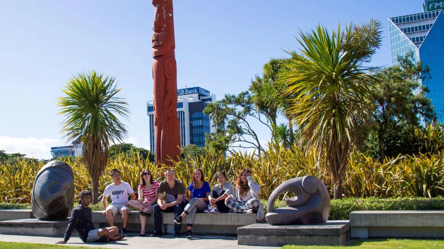 Students sitting near Pouwhenua Māori carving in The Square