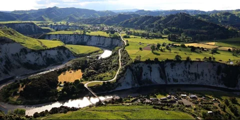 Aerial view of Mangaweka’s scenic white cliffs and the Rangitīkei River with Awastone Campground surrounded by green hills in Manawatū, New Zealand