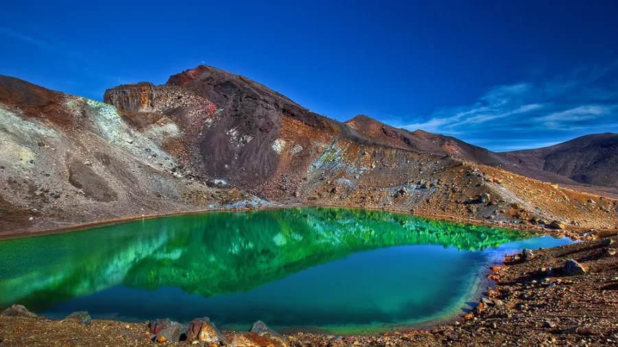 A vibrant green Emerald Lake reflecting the sky and volcanic slopes on the Tongariro Alpine Crossing in New Zealand.