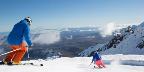 Skiers descending Whakapapa Ski Area with volcanic summit views