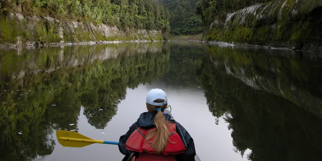 Woman canoeing down a calm stretch of the Whanganui River in the morning mist
