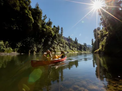 Canoeists on the Whanganui River paddling through sunlight-dappled water