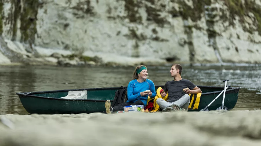 Couple enjoying a picnic by their canoe on the Whanganui River Journey