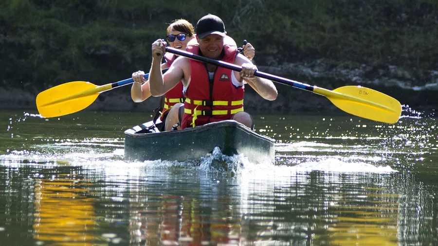 Two people paddling a canoe on the Whanganui River wearing life jackets