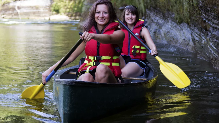 Two women smiling as they paddle a canoe on the Whanganui River