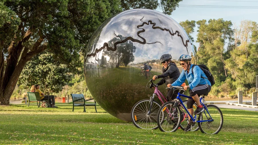 Cyclists riding past the shiny metal dome sculpture Te Pātaka o Roto Moko in Whanganui