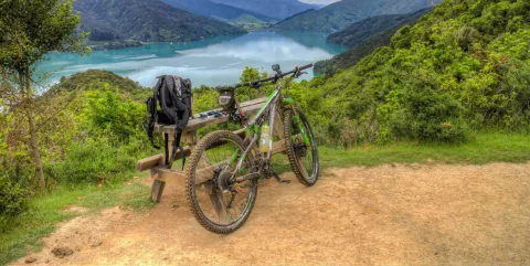 Mountain bike resting against a bench uphill from Anakiwa with views over Kenepuru Sound